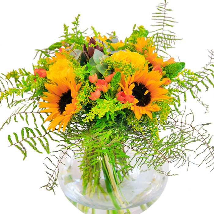 The first glance at this bouquet conjures visions of golden afternoons on local Manor House greenways-sunflowers, with their signature dark centers and vibrant, sunbeam-tipped petals, take pride of place amid a lavish collection of garden roses in mellow yellow hues. The roses' tightly whorled petals radiate outward in gentle spirals, adding depth and an old-world romance, while clusters of gleaming red Hypericum berries pop among the greenery, suggesting cherries ripening in a late summer sun. Layers of lush foliage, including airy, feathery ferns, cascade lightly over the edge of the vase, echoing the movement of grass on breezy Parkland Walks. Slender green spikelets and sprays of goldenrod highlight the wild, natural spirit of the arrangement, while scattered eucalyptus leaves bring a cooling undertone, their blue-green surfaces catching glimmers of daylight. The round glass vase, crystal clear, reveals tangled stems reaching down into the freshness of water, a detail that underscores the local florist's craftsmanship and passion for natural presentation. Each floral element-downy sunflower, smooth rose, crisp foliage-invites curiosity, promising a bouquet that delights both sight and touch. This arrangement, glowing with warmth and harmony, is perfect for brightening up homes or offices across Manor House or for adding heartfelt brightness to celebrations, be they birthdays, anniversaries, or joyful reunions along Seven Sisters Road.